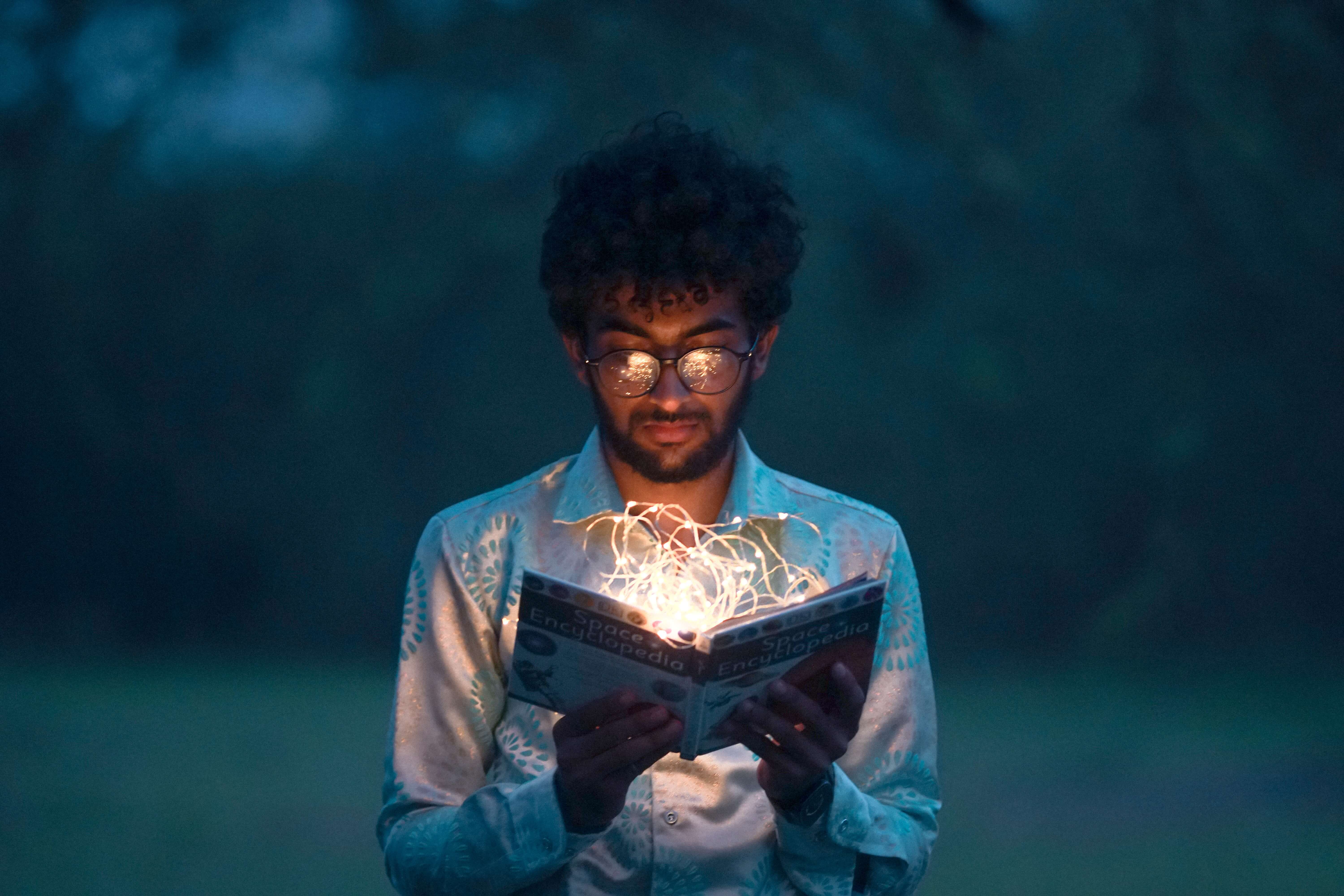 Jongeman met zwarte krulletjes leest lichtgevend boek