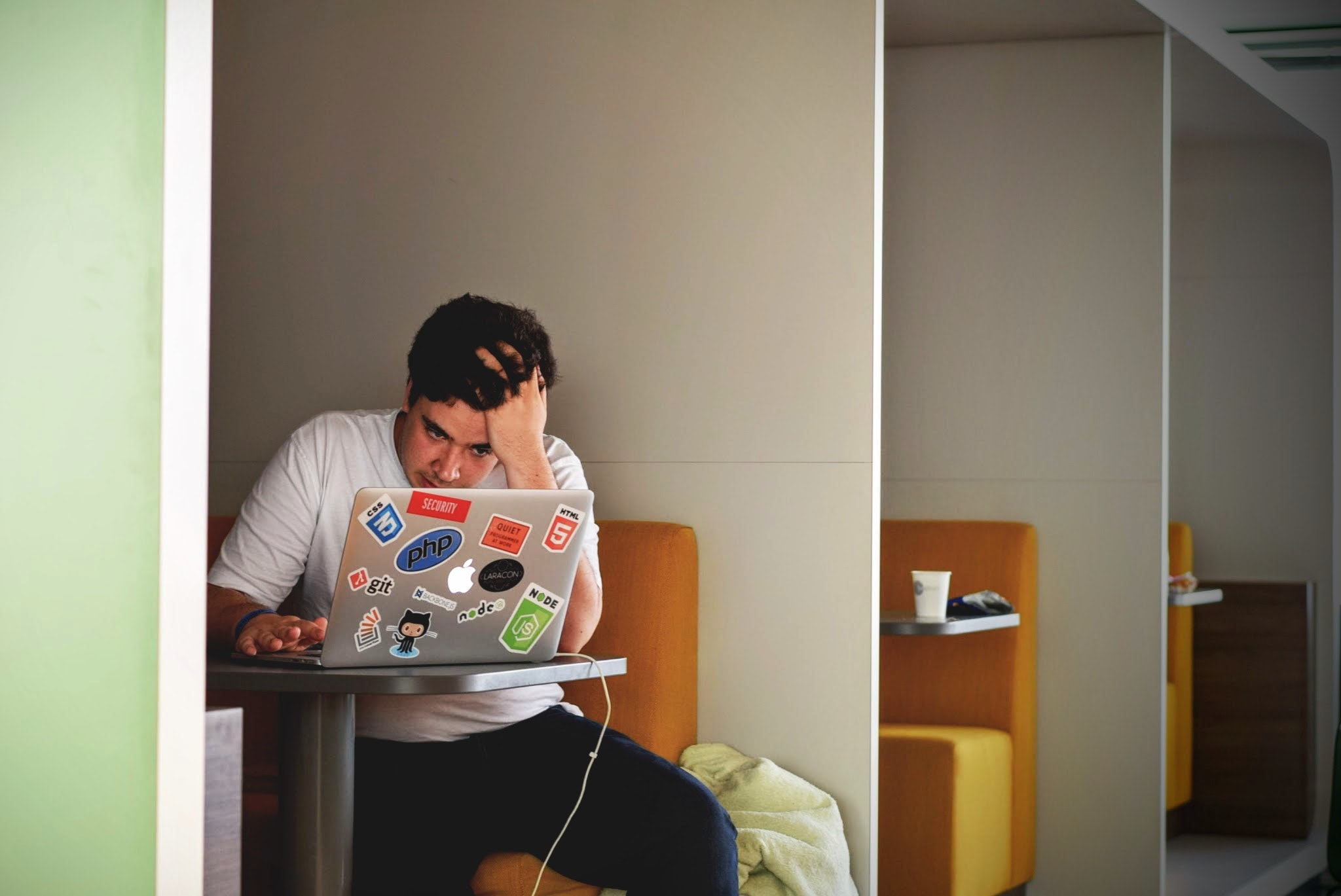 Jongeman studeert met laptop in studieruimte, zit met hand in zijn haar