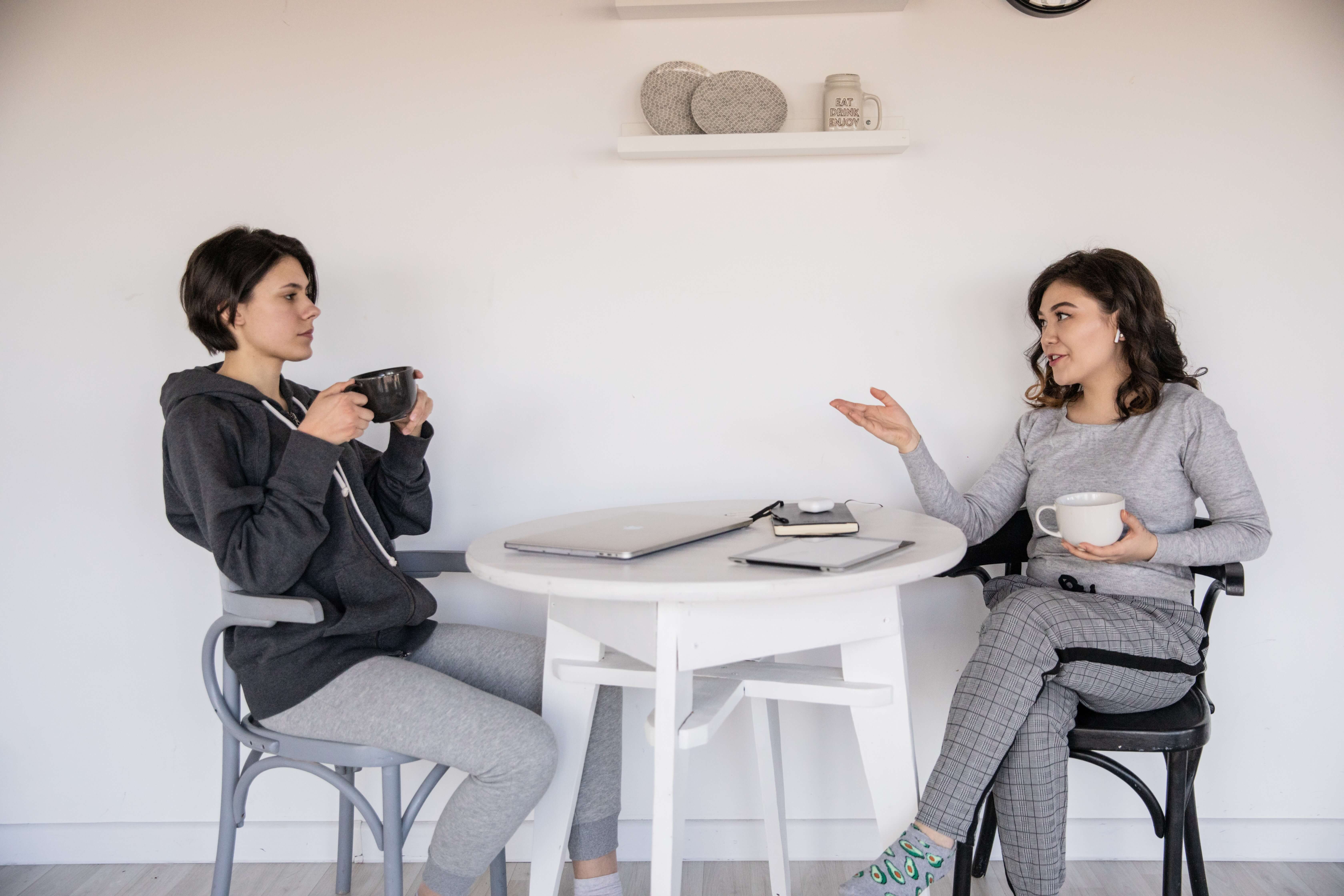 Twee vrouwen in grijze kleren praten aan koffietafel