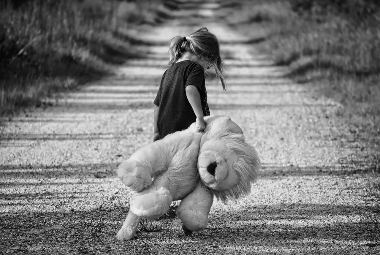 Zwart-witfoto van verdrietig meisje dat grote leeuwenknuffel achter zich aan sleept