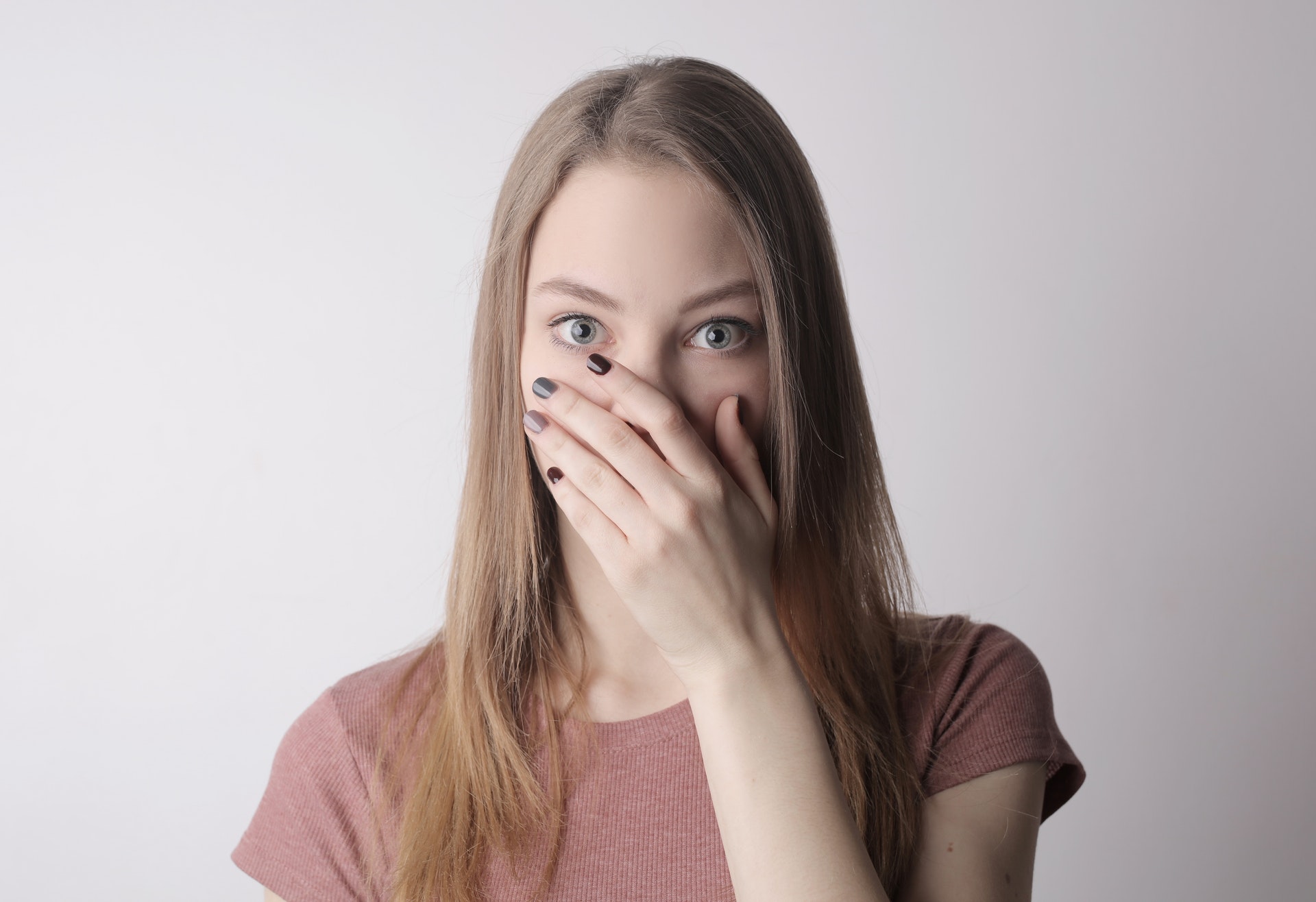 Jonge vrouw in zachtroze t-shirt slaat bang de hand voor de mond