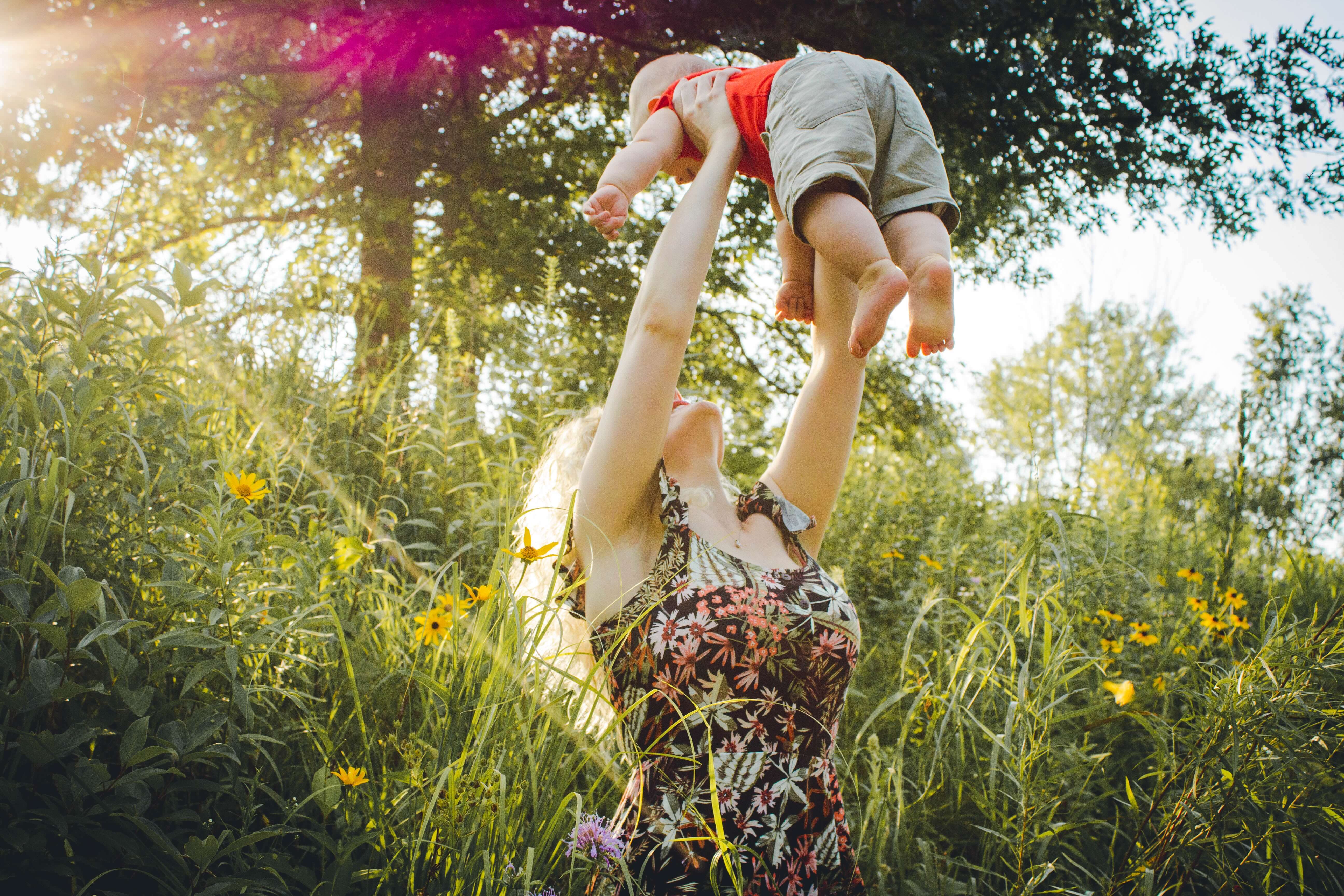 Mama gooit peutertje in de lucht in veld met heel hoge grassen