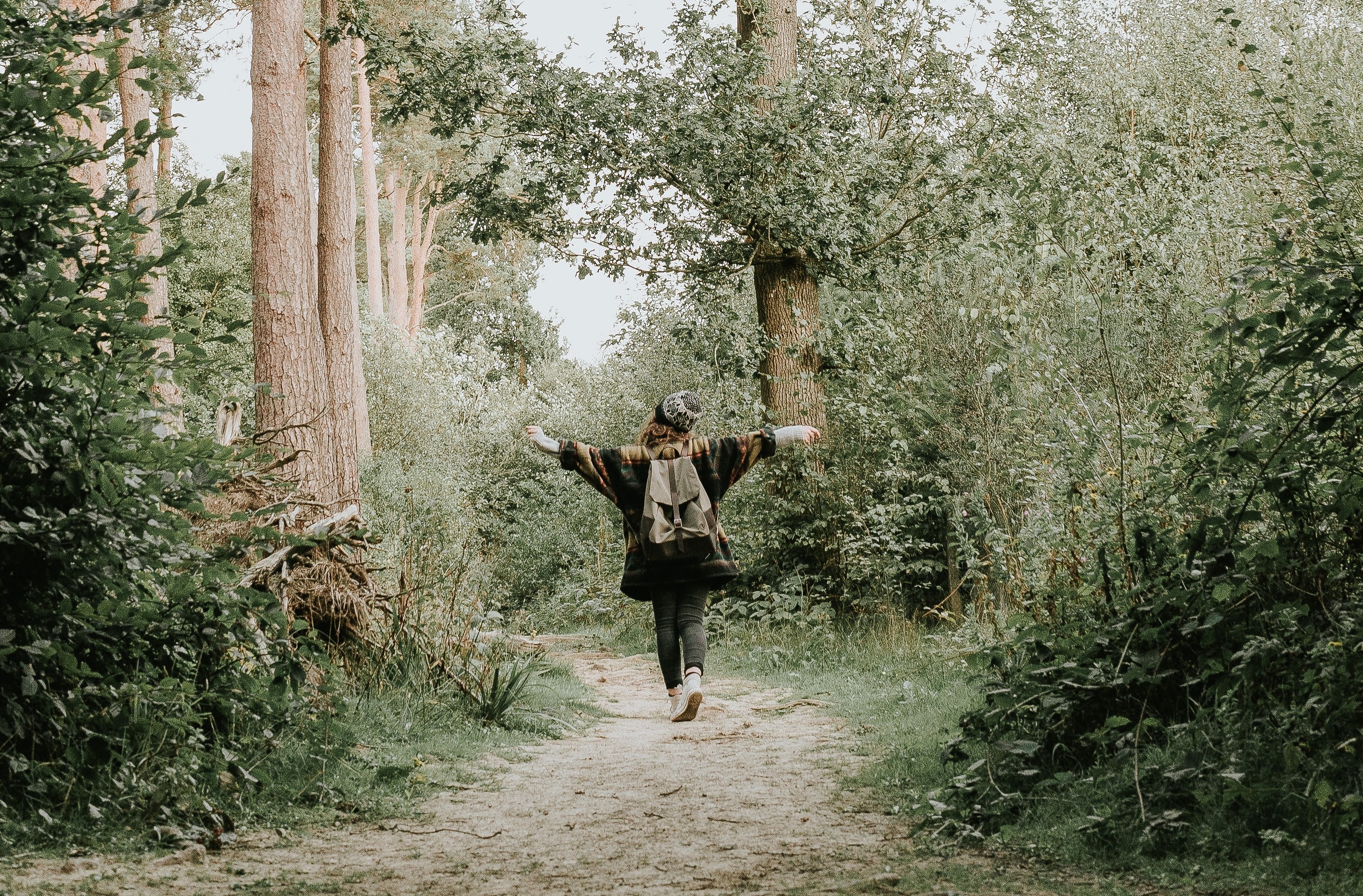 Meisje met rugzak en muts wandelt op een bospad met haar armen wijd