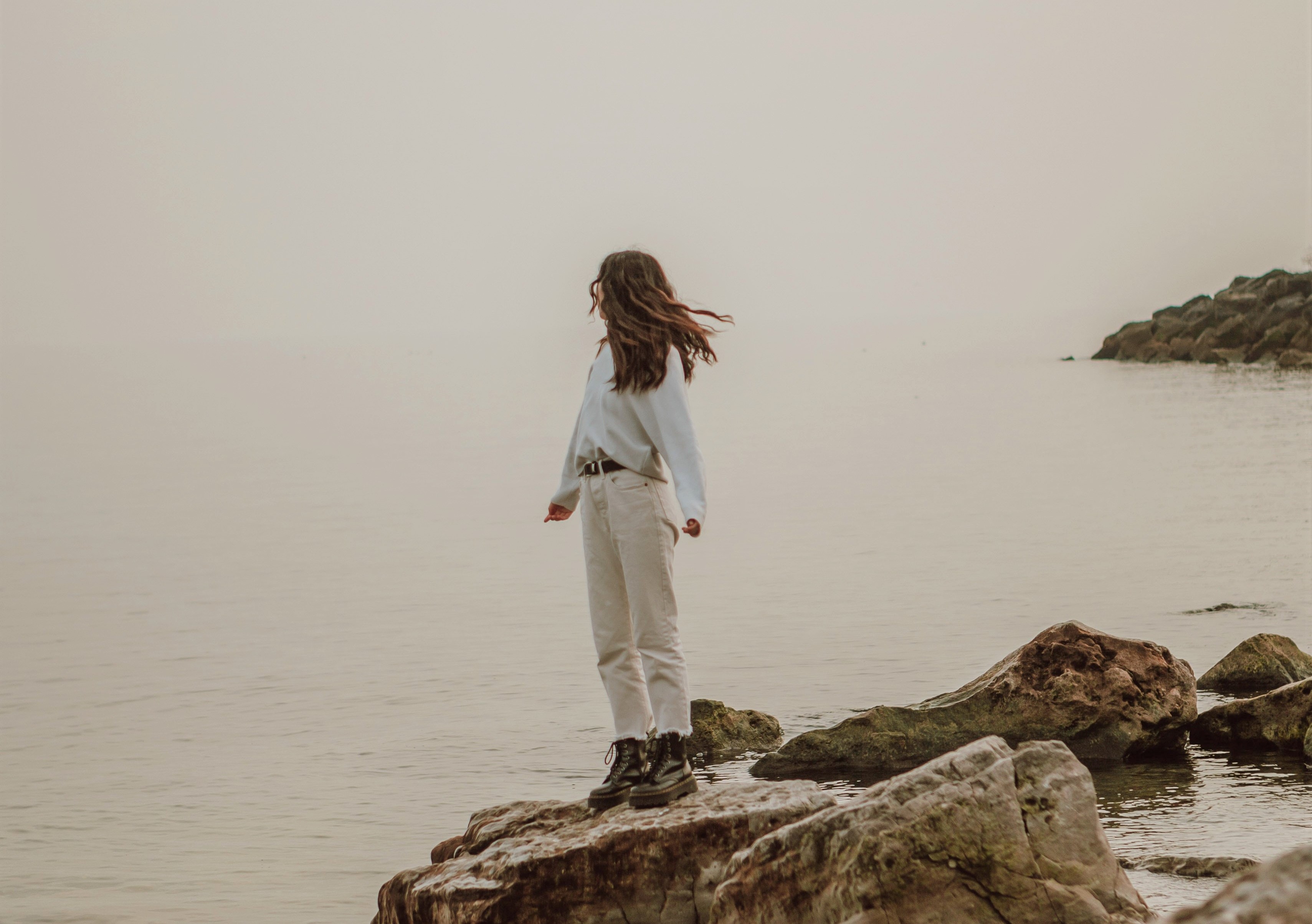Meisje met lang bruin haar staat op rots en kijkt naar de zee