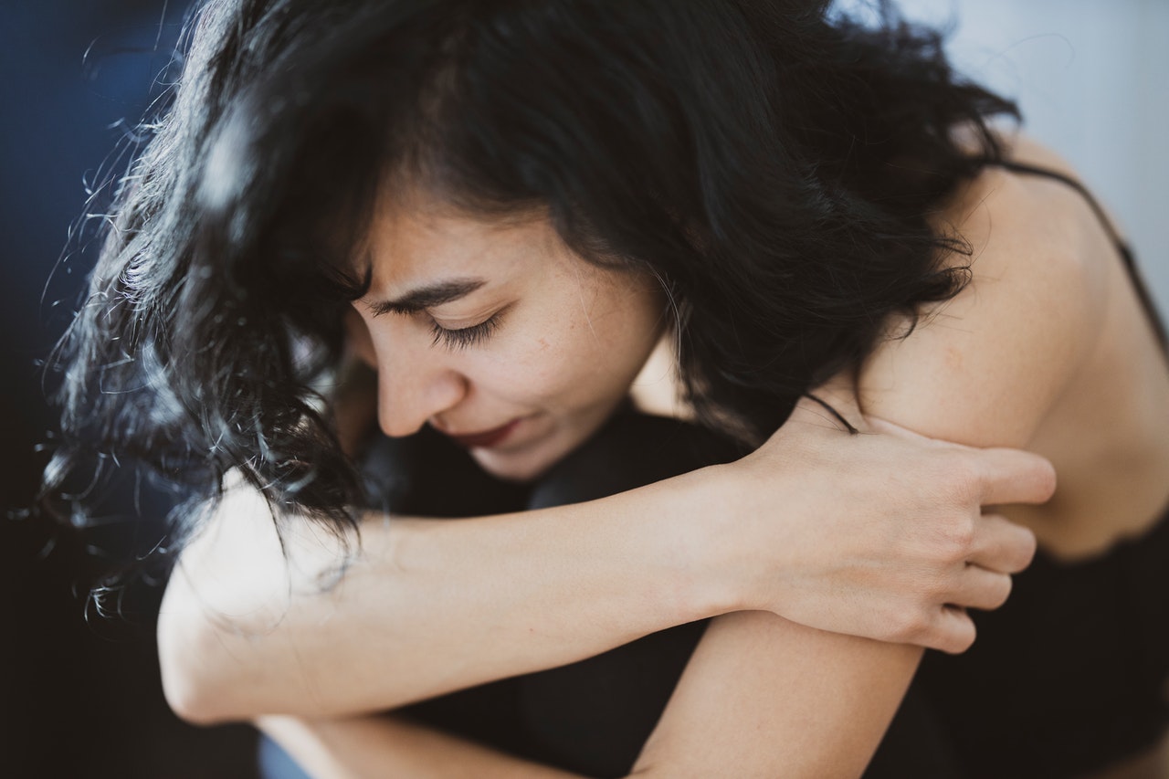 Vrouw met zwart haar zit in elkaar gedoken en houdt haar armen vast