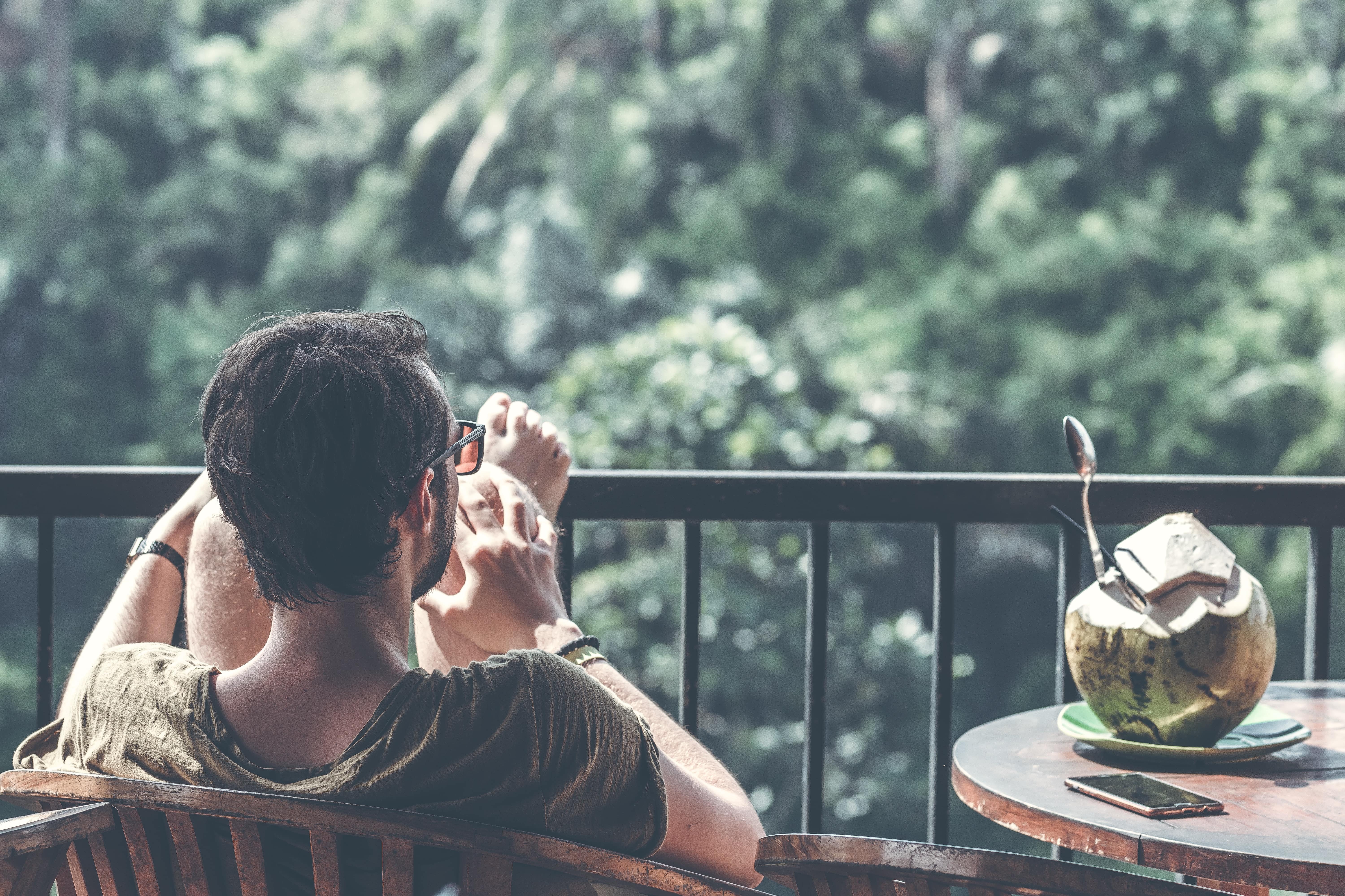 Man kijkt op het groen uit vanop zijn balkon. Op het tafeltje rechts staat een opengemaakte kokosnoot