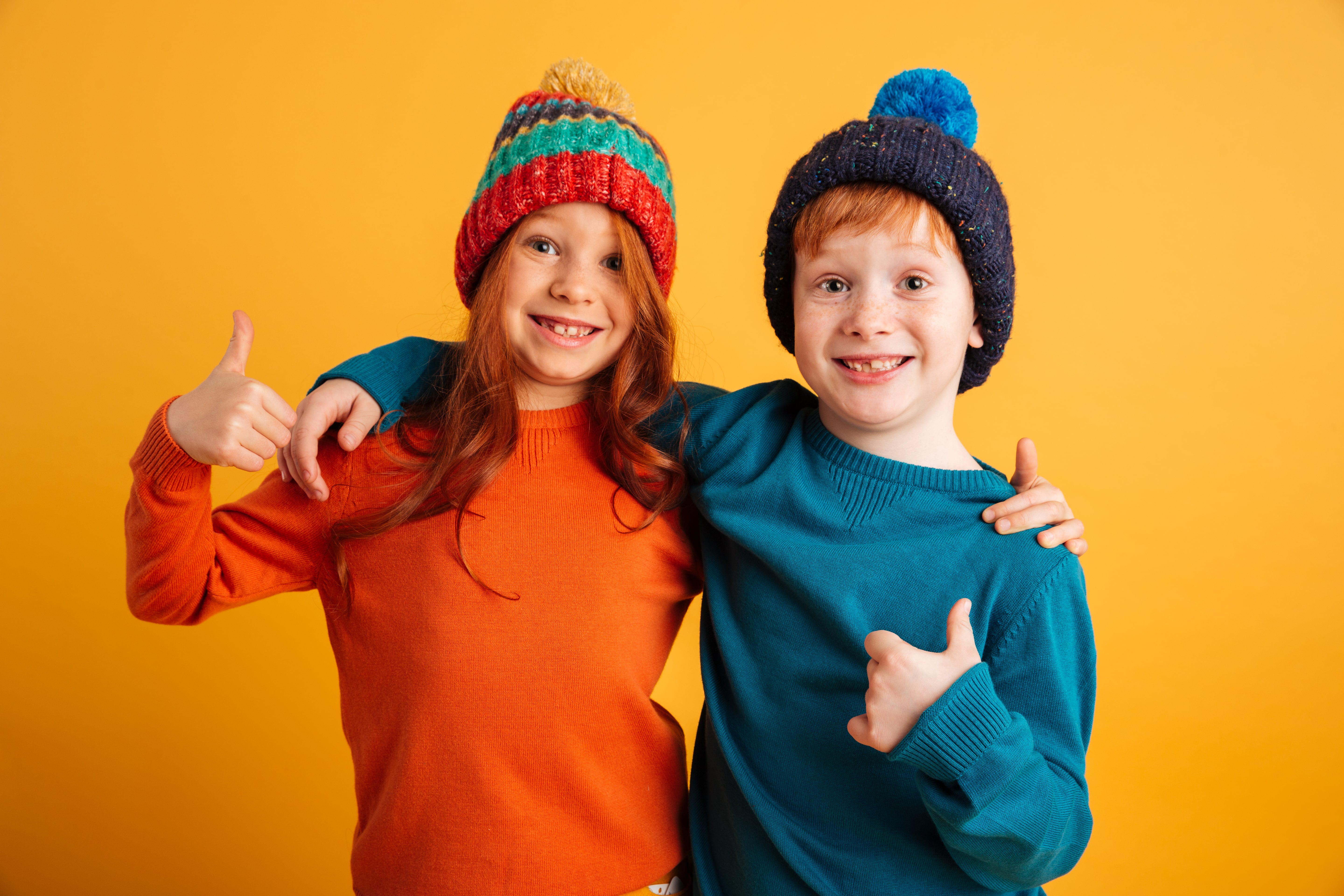 Ros jongen en meisje met kleurrijke mutsen steken grijzend en enthousiast hun duimen op