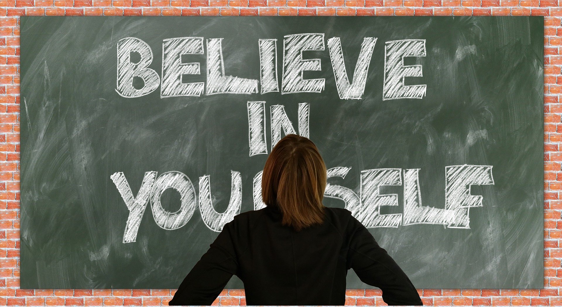 Vrouw kijkt naar krijtbord met tekst believe in yourself