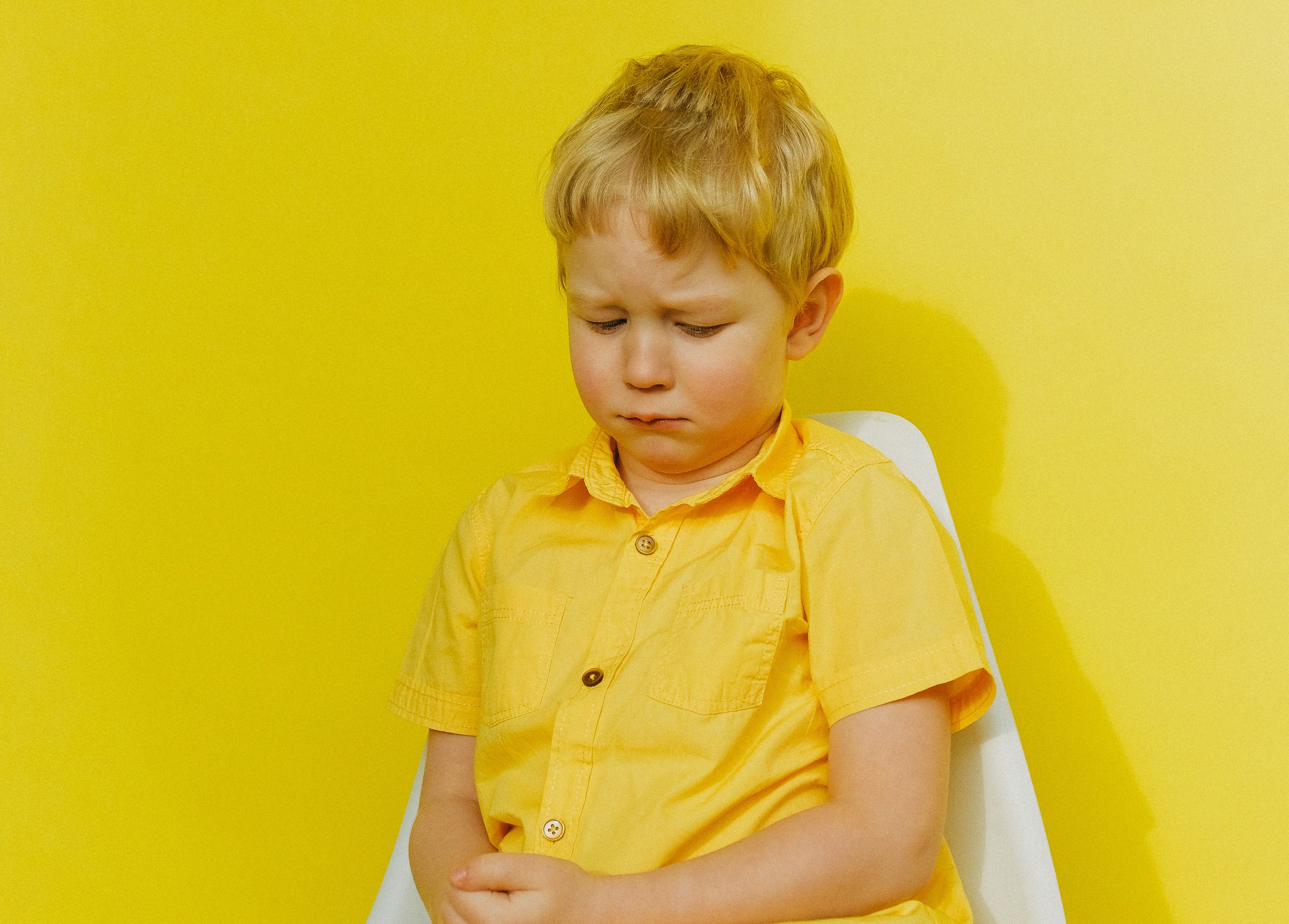 Blond jongetje in geel shirt tegen gele achtergrond kijkt verdrietig