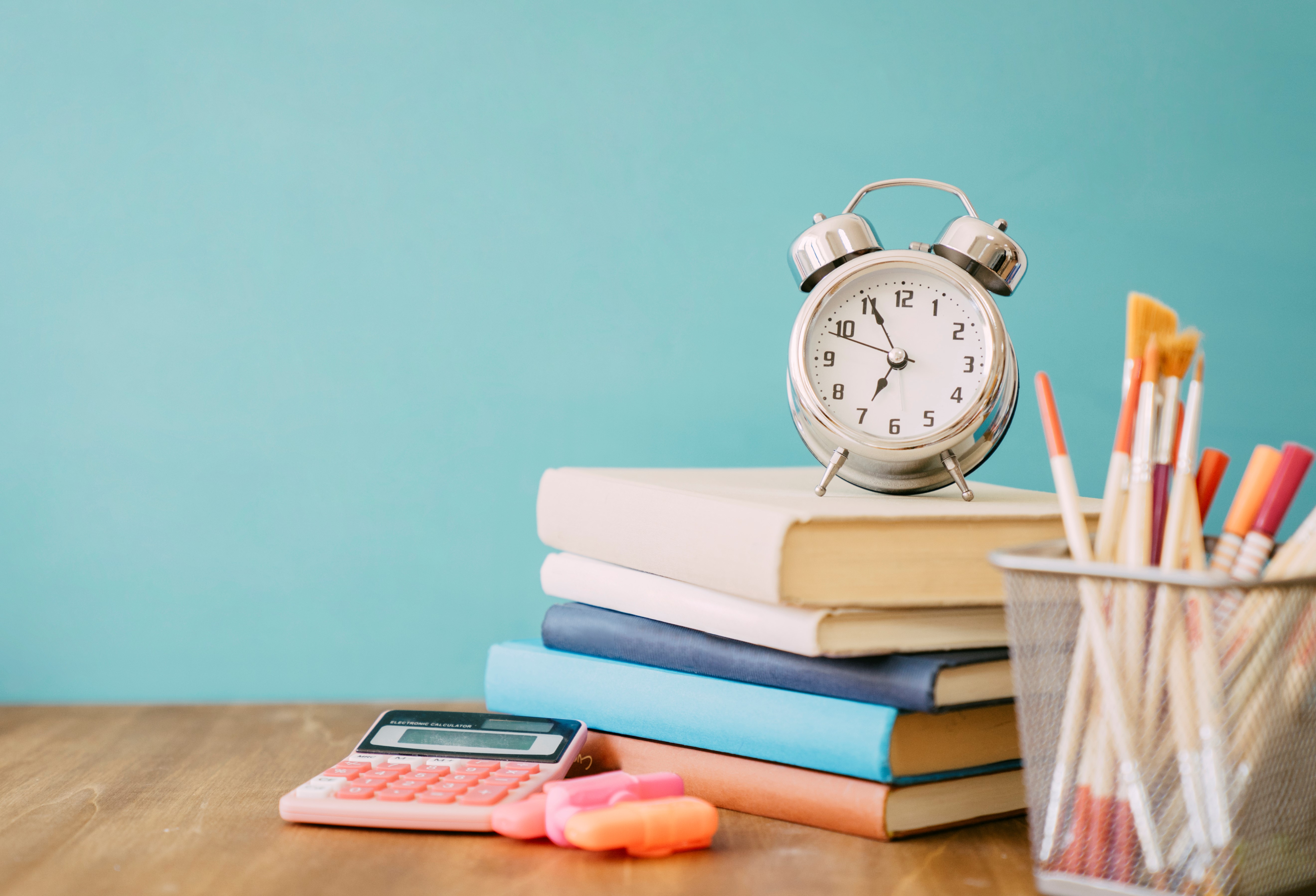 Stapel boeken op bureau met analoog klokje, pennenpot en rekenmachine