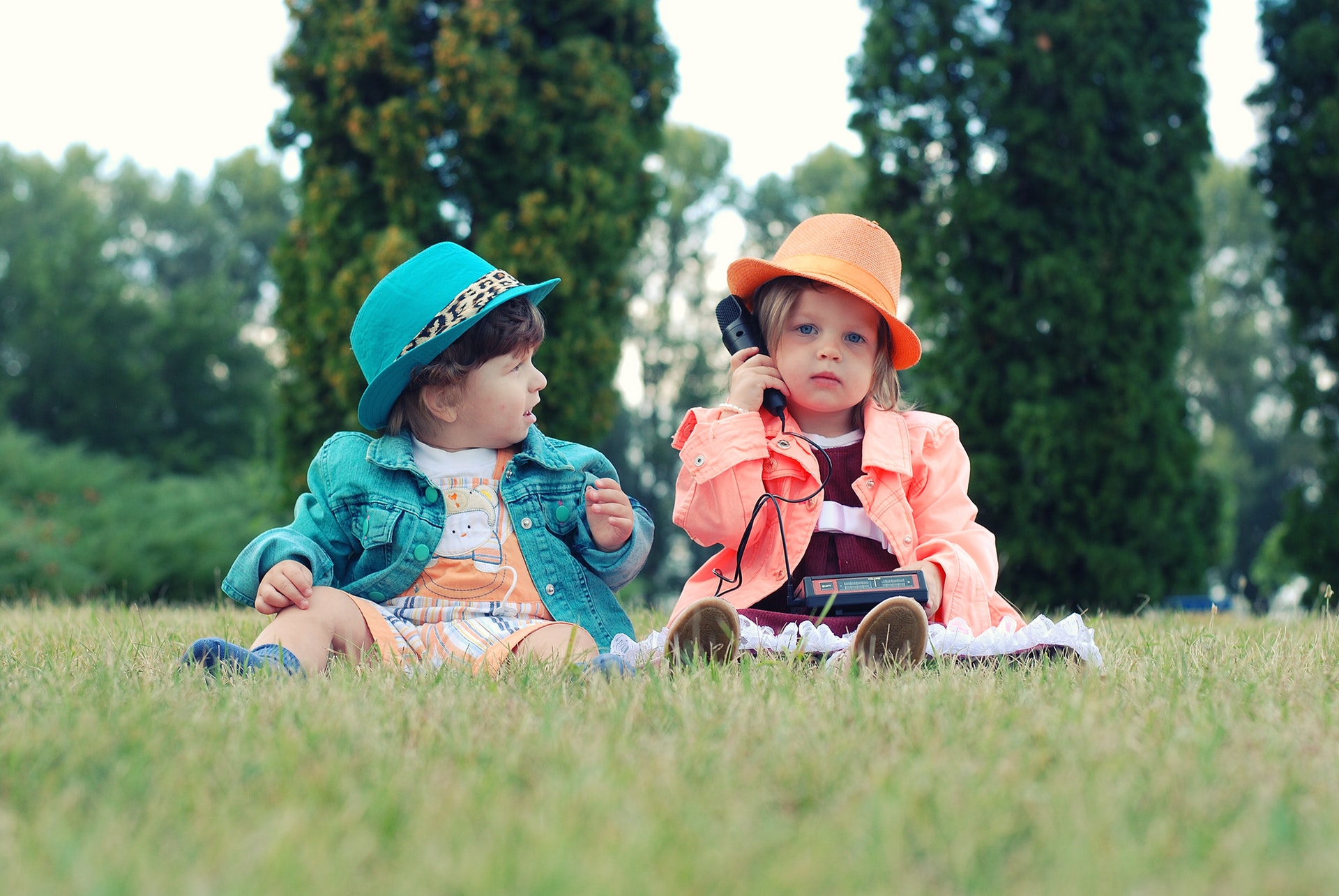 Twee kindjes met hoedjes in het gras spelen met speelgoedtelefoon
