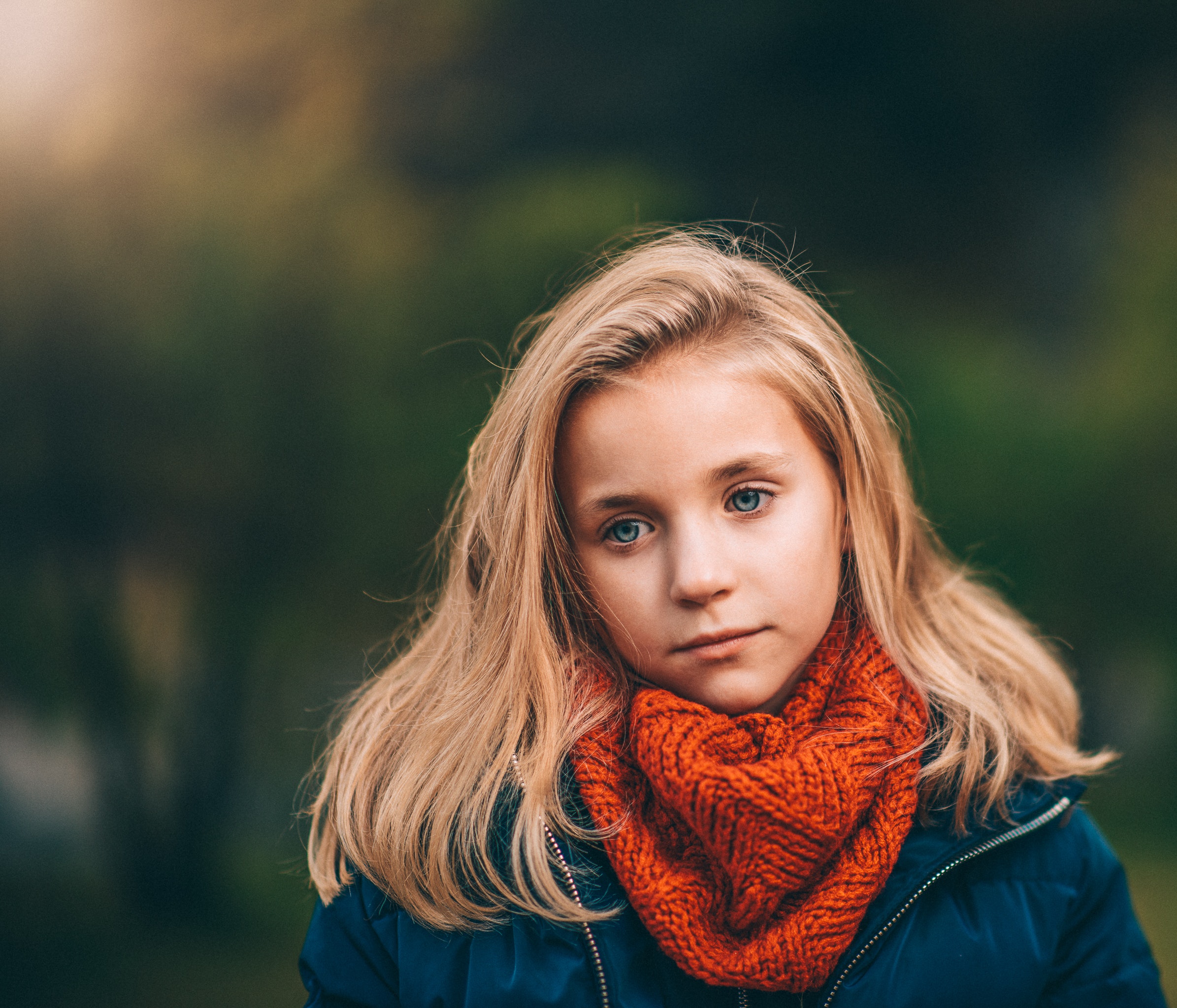 Meisje met oranje sjaal en blond haar staart voor zich uit