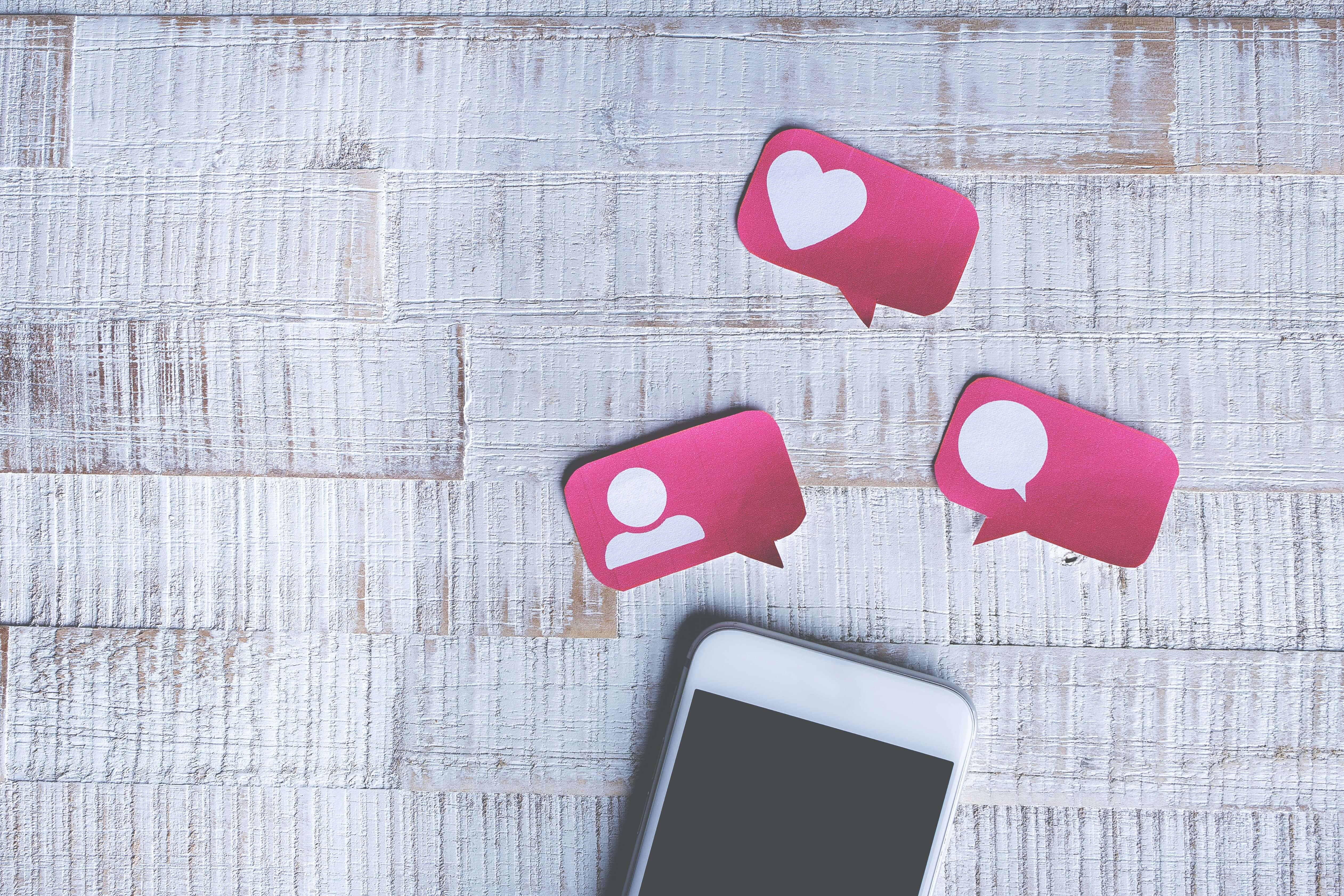 Smartphone op tafel met tekstballonnetjes erboven met hartje, persoontje en tekstballonnetje