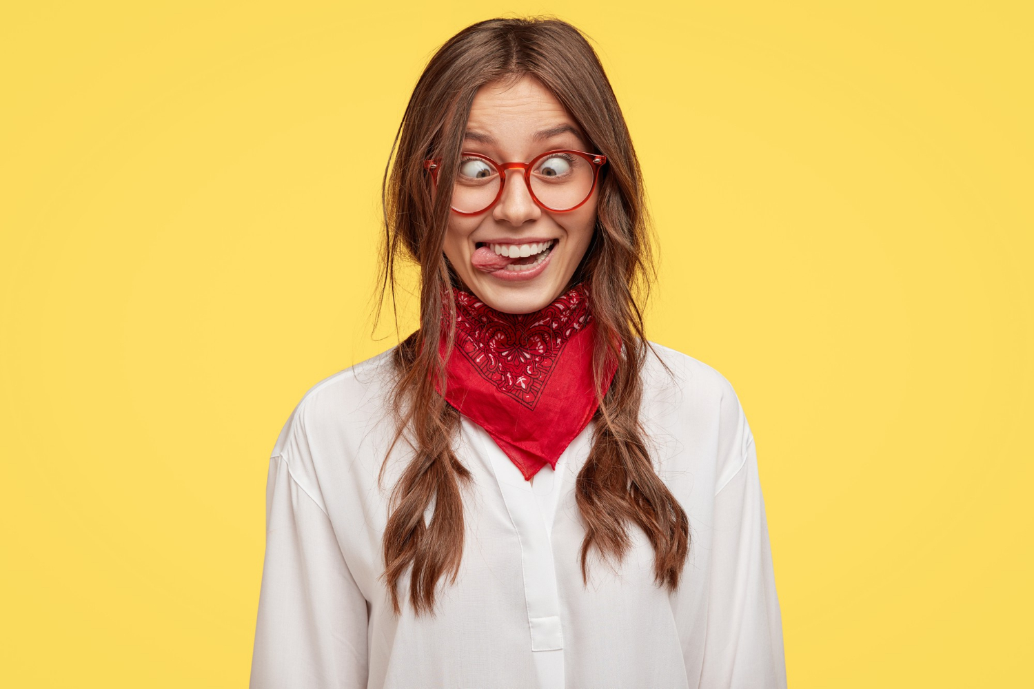 Vrouw met rode bril en rood sjaaltje tegen gele achtergrond trekt gek gezicht
