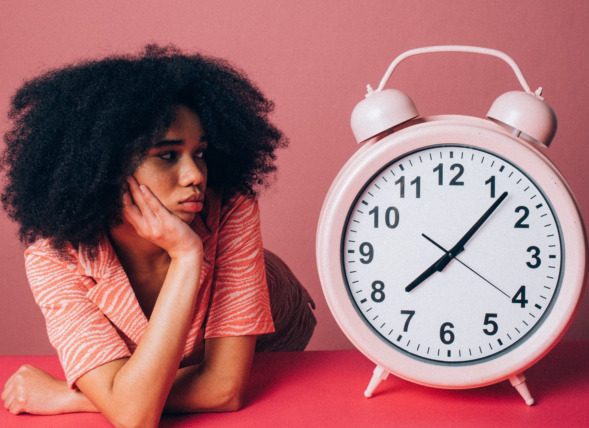 Zwarte vrouw in roze shirt kijk bedrukt naar reuzegrote roze alarmwekker