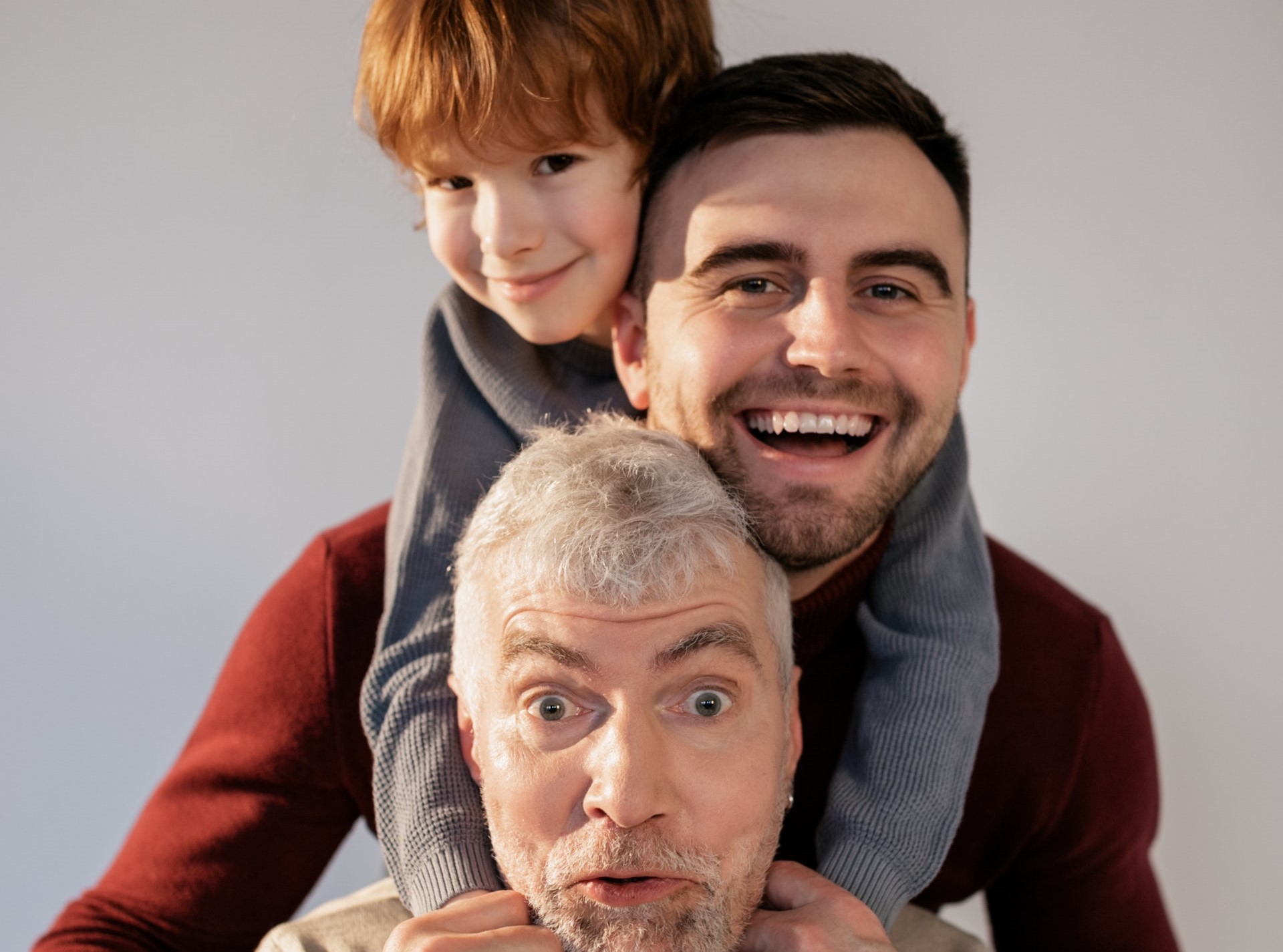 Grootvader met wit haar, daarachter papa met baard en zwart haar en op zijn schouders zoontje met ros haar