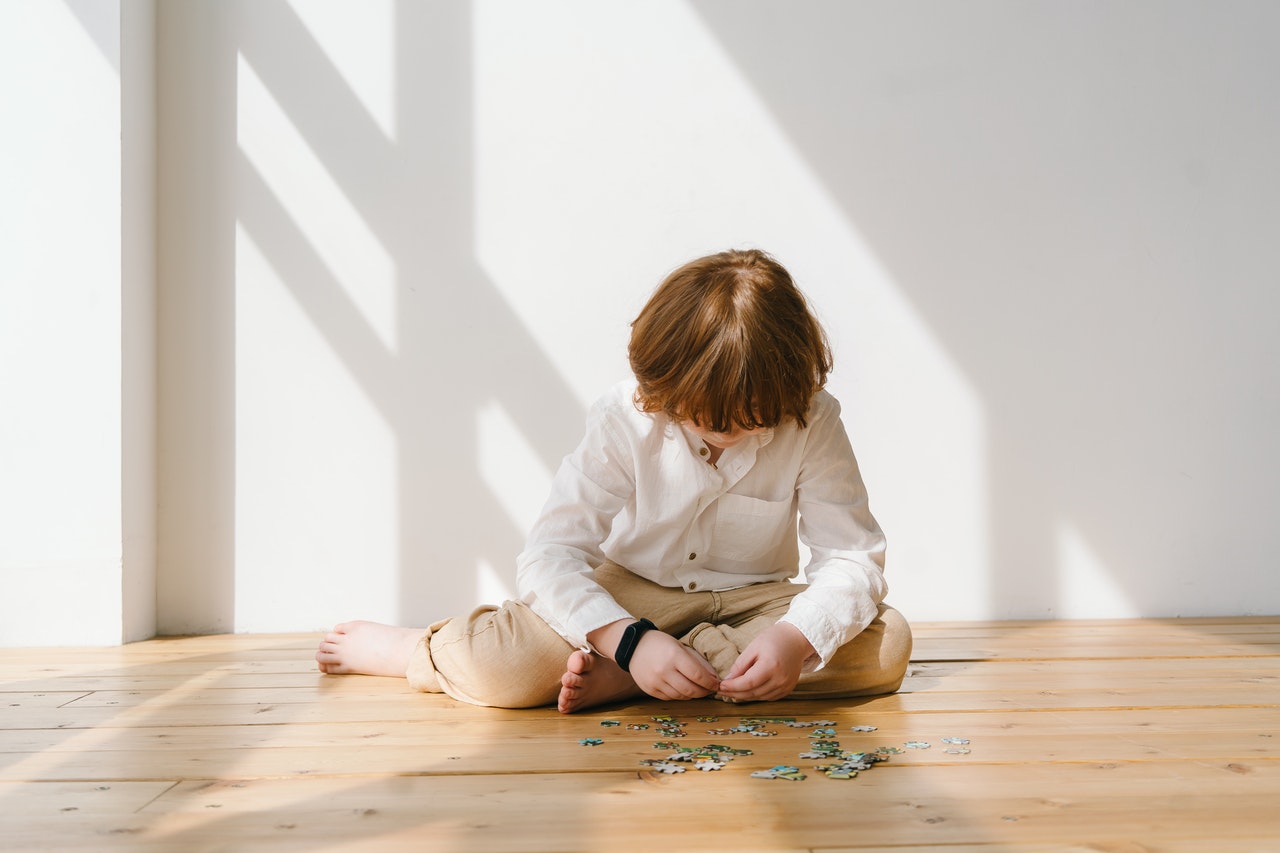 Jongen in wit hemd puzzelt op parketvloer naast een raam