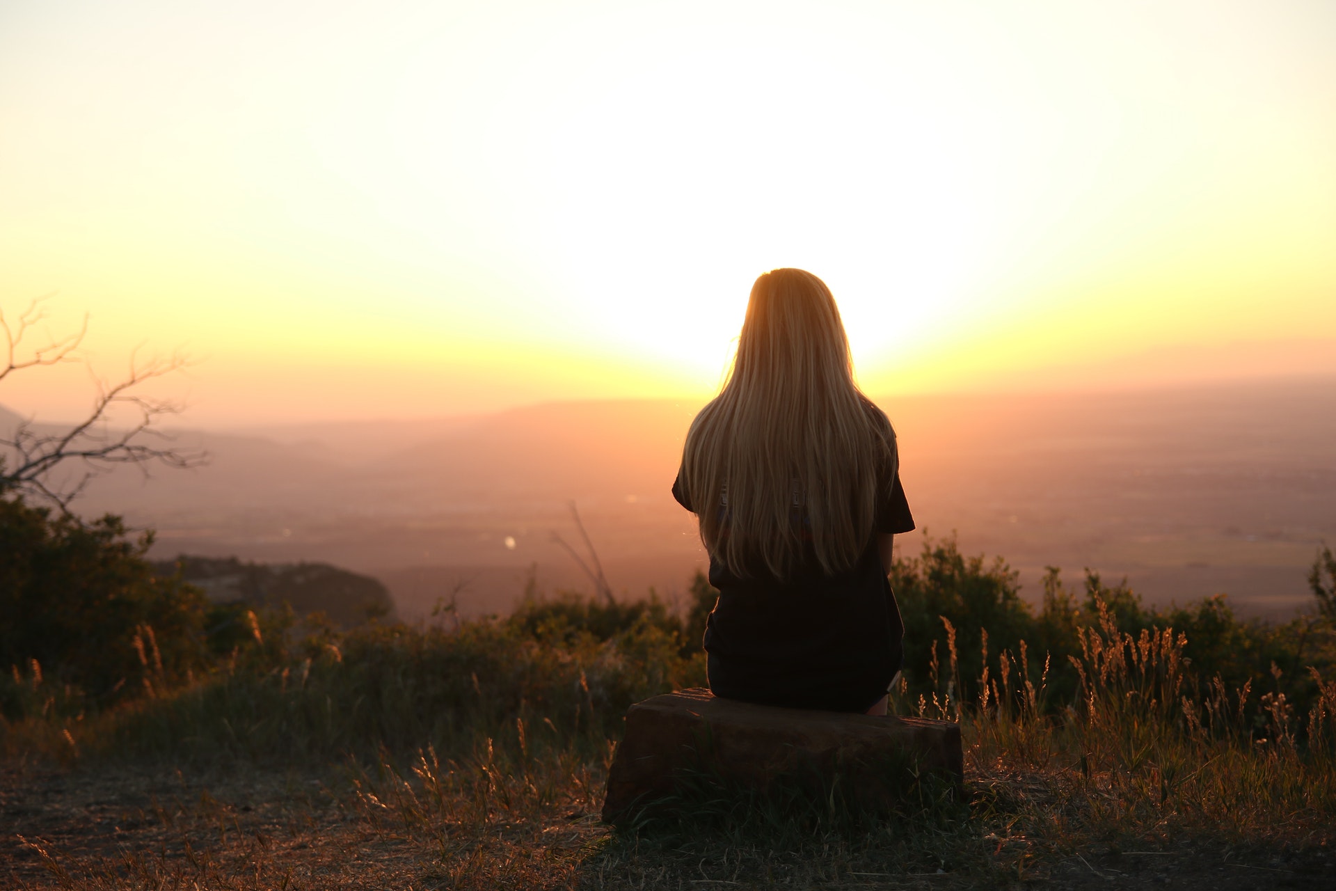 Vrouw kijkt over landschap naar ondergaande zon